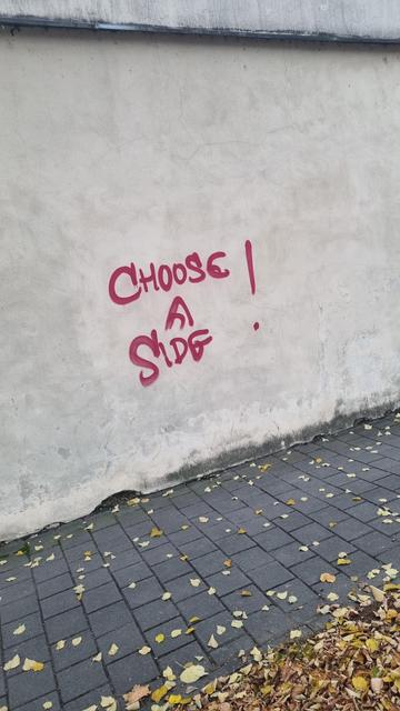 A graffiti saying, choose a side
 White wall red letters