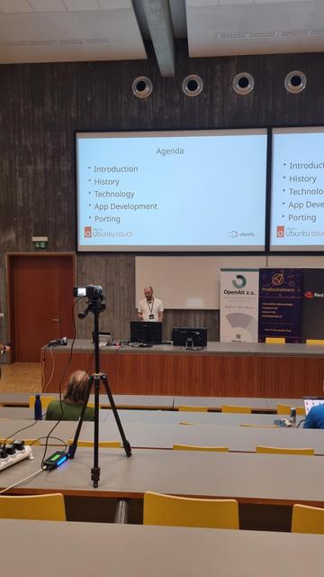 A white male on a stage. Camera is also visible.