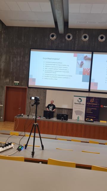 White male in front of a screen. The screen is about MapComplete.