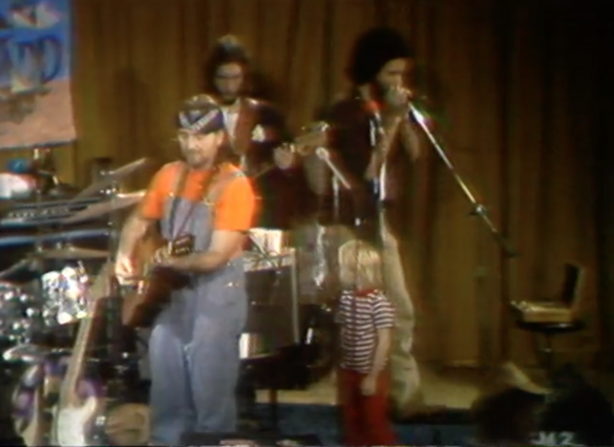 Willie Nelson with small child onstage looking on