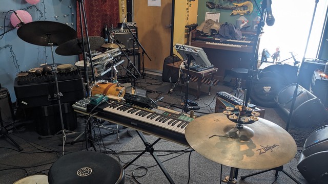 Room full of gear, including keyboards, drums, harmonium