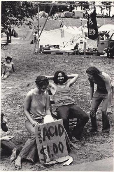 couple sits behind sign reading Acid $1.00