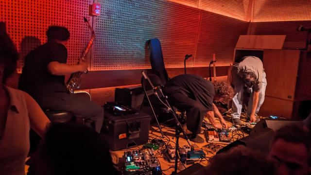 musicians packing up after gig, many pedals onstage