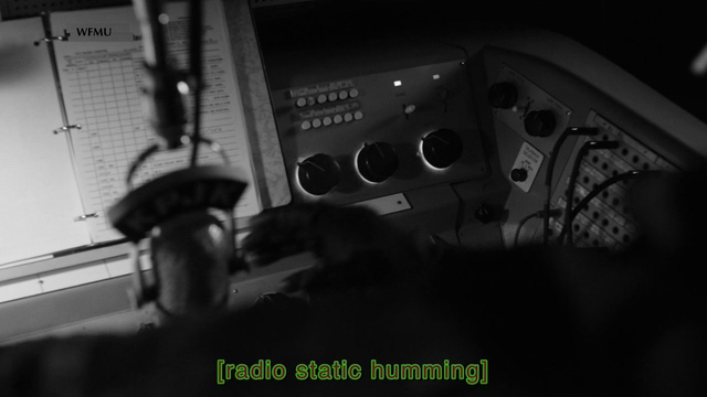 screencap from Twin Peaks: The Return, with a hand reaching towards microphone & caption [radio static humming]