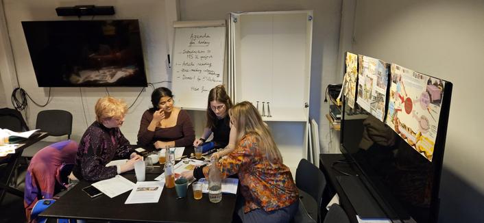 People making a collage at a table with cups and bottles. On a TV beside them are several collages taped to cover the TV.