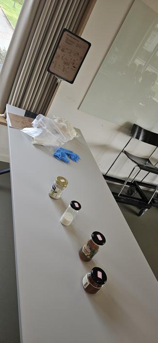 A long table with different types of jars with small labels on top. In the background is a bag of mushroom-growing starter and guides