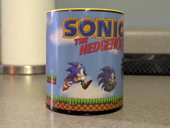 A Sonic the Hedgehog mug that's color changed. There is a blue sky and logo.