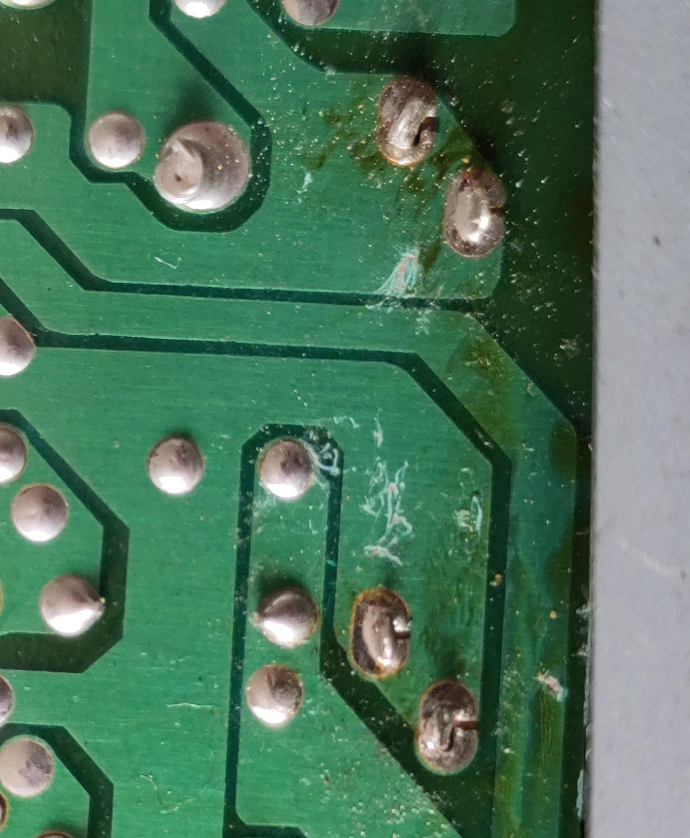 Nærbillede af en grøn printplade. Nogle gennemførte forbindelser er mere eller mindre fri for loddetin, men ind i mellem dem ses  lyse kradsemærker på overfladen.