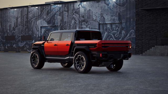 Red and black GMC Hummer EV pickup parked on pavement in front of a wall covered in a black-and-white urban graffiti mural, shown from a rear three-quarter angle.