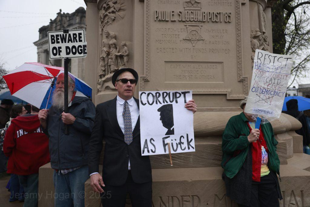 Protestors at the Monroe County Courthouse. One is holding a sign saying "Corrupt as futk"