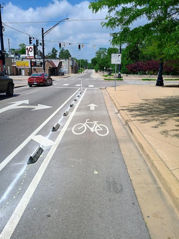 A bike lane at 3rd and Eagleson in Bloomington, IN. It's separated from two lanes of 30MPH one-way traffic by a series of six-inch high rubber barriers. 