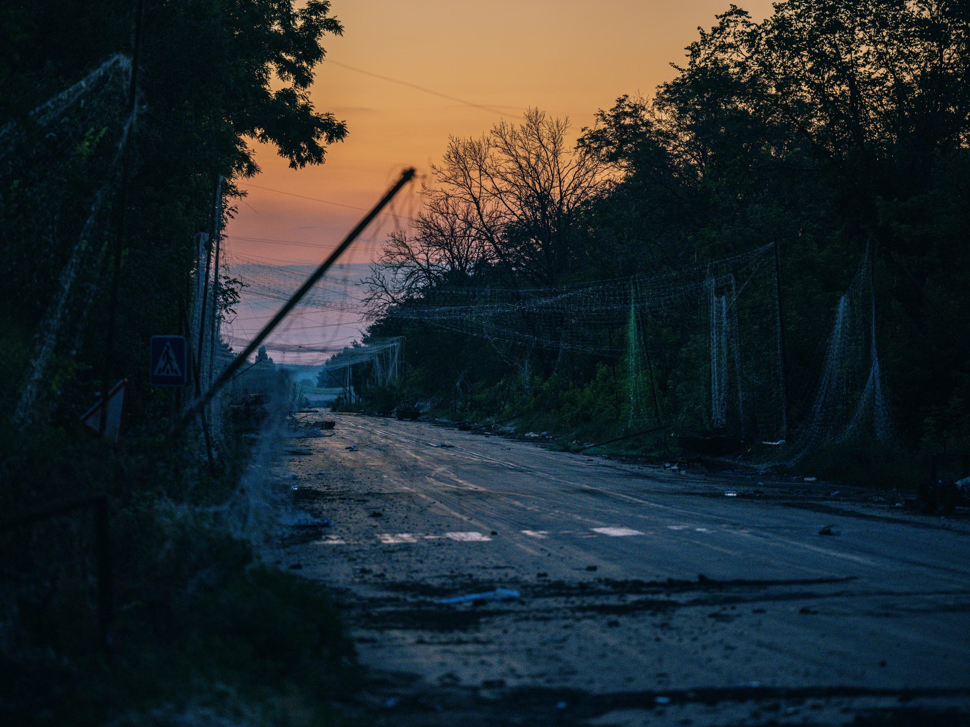 A battered road in the countriside in the sunset. The Guardian caption: ’ The road to Kostyantynivka covered with anti-drone nets. ’
