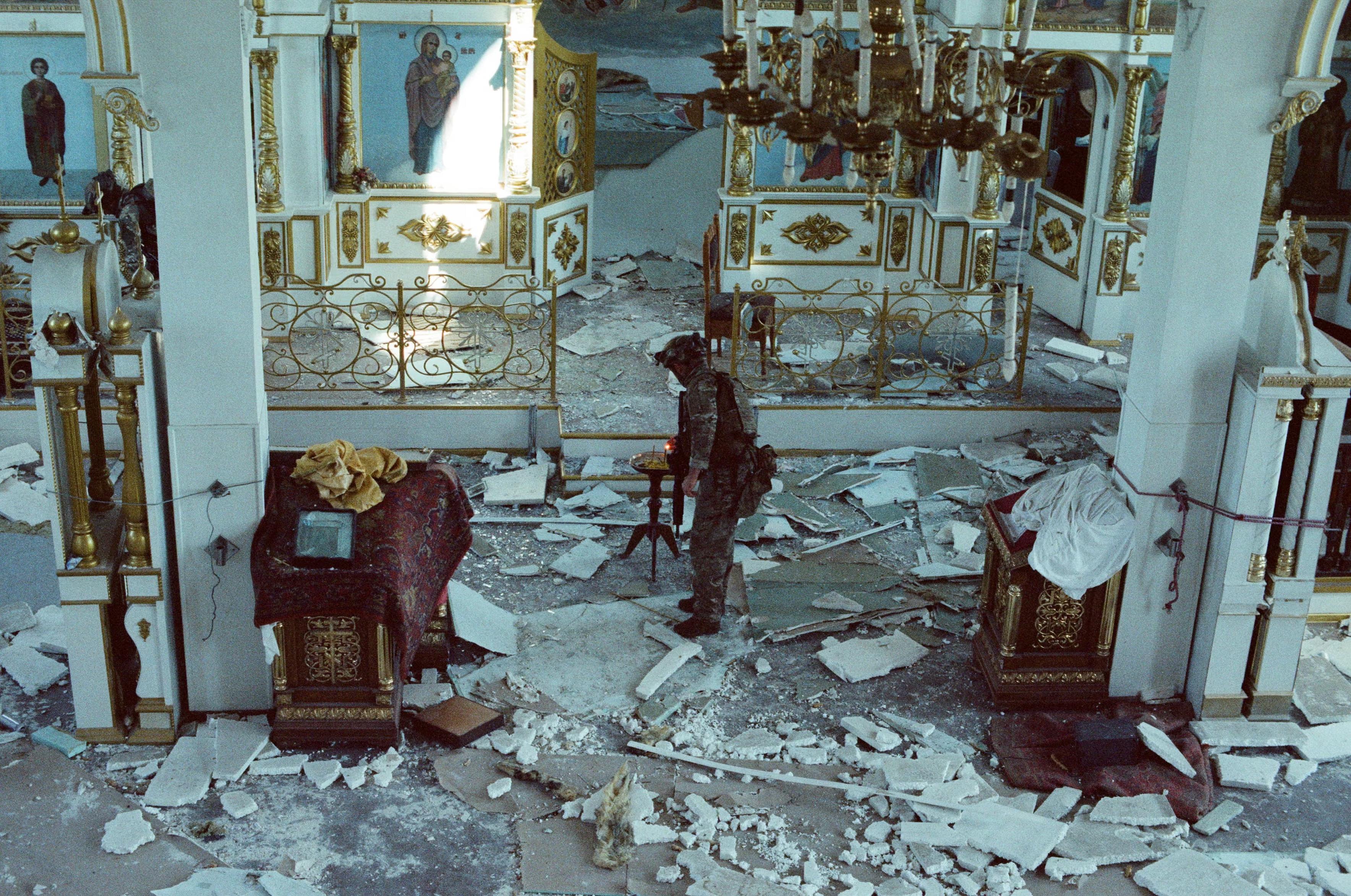 The Guardian caption: ’ Dzhango lighting a candle in a damaged church ’
