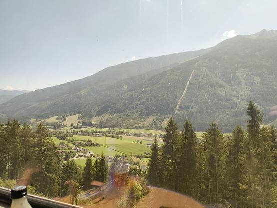 Zu sehen ist ein Foto, aufgenommen aus einem Zugfenster auf die österreichischen Alpen.