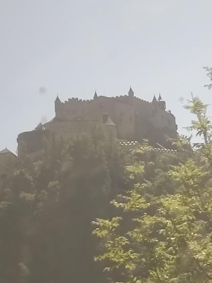 Zu sehen ist ein Foto, aufgenommen aus einem Zugfenster auf eine Burg in den österreichischen Alpen.