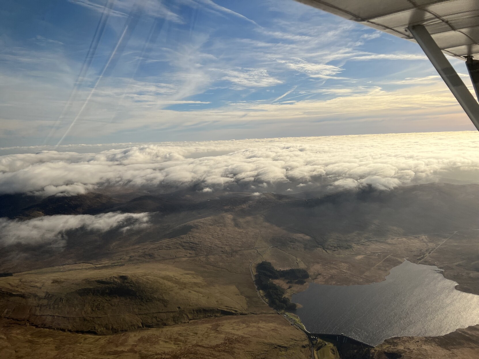 A layer of fluffy clouds setting above the Mourn Mountains. The photo looks down on top of the clouds.