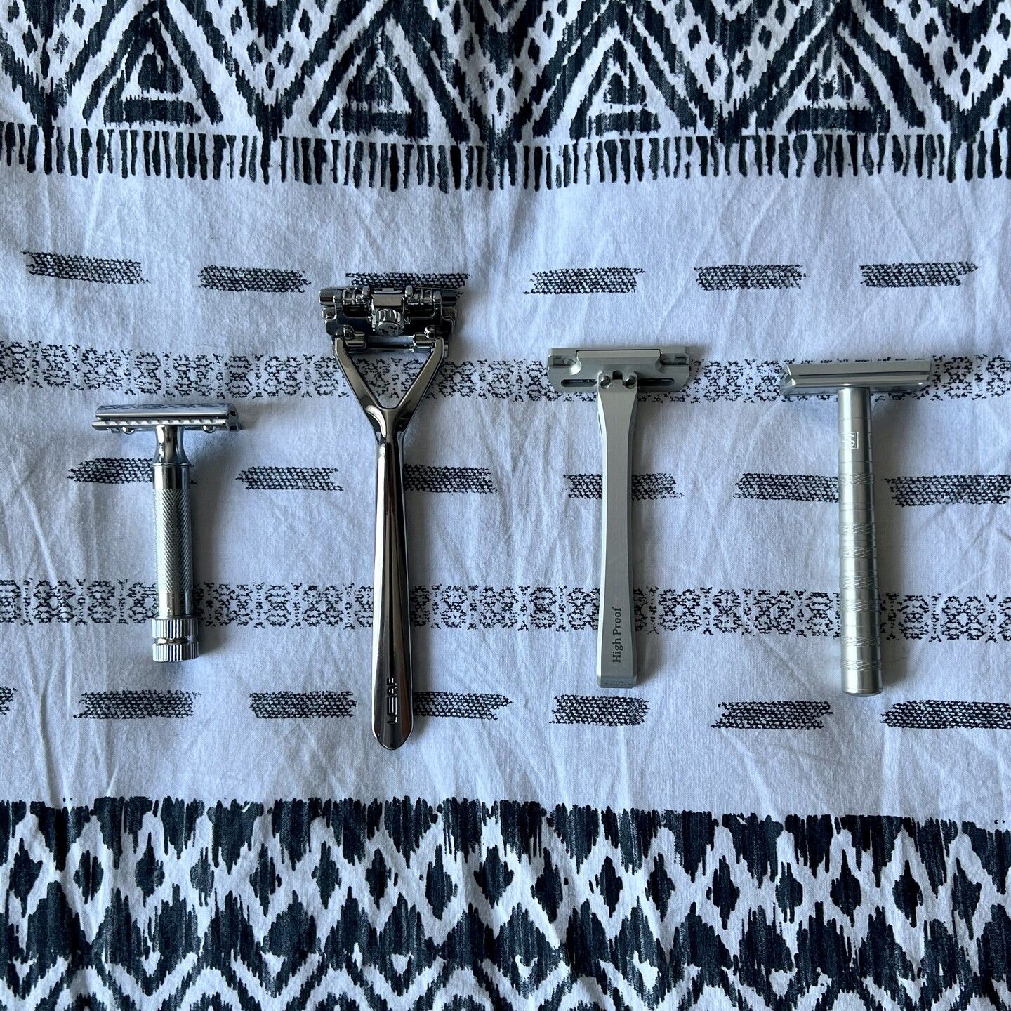 Four different safety razors laid out on a black and white sheet. Photo taken from directly above.