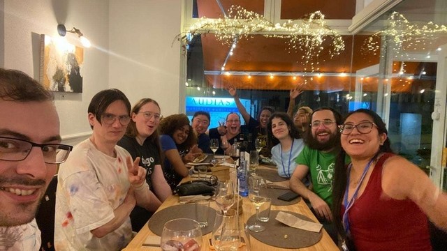 A group of people sitting at a restaurant table posing for a selfie and smiling. 