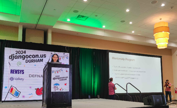 woman speaking at a podium with a backdrop of "2024 django con US durham" behind her. 