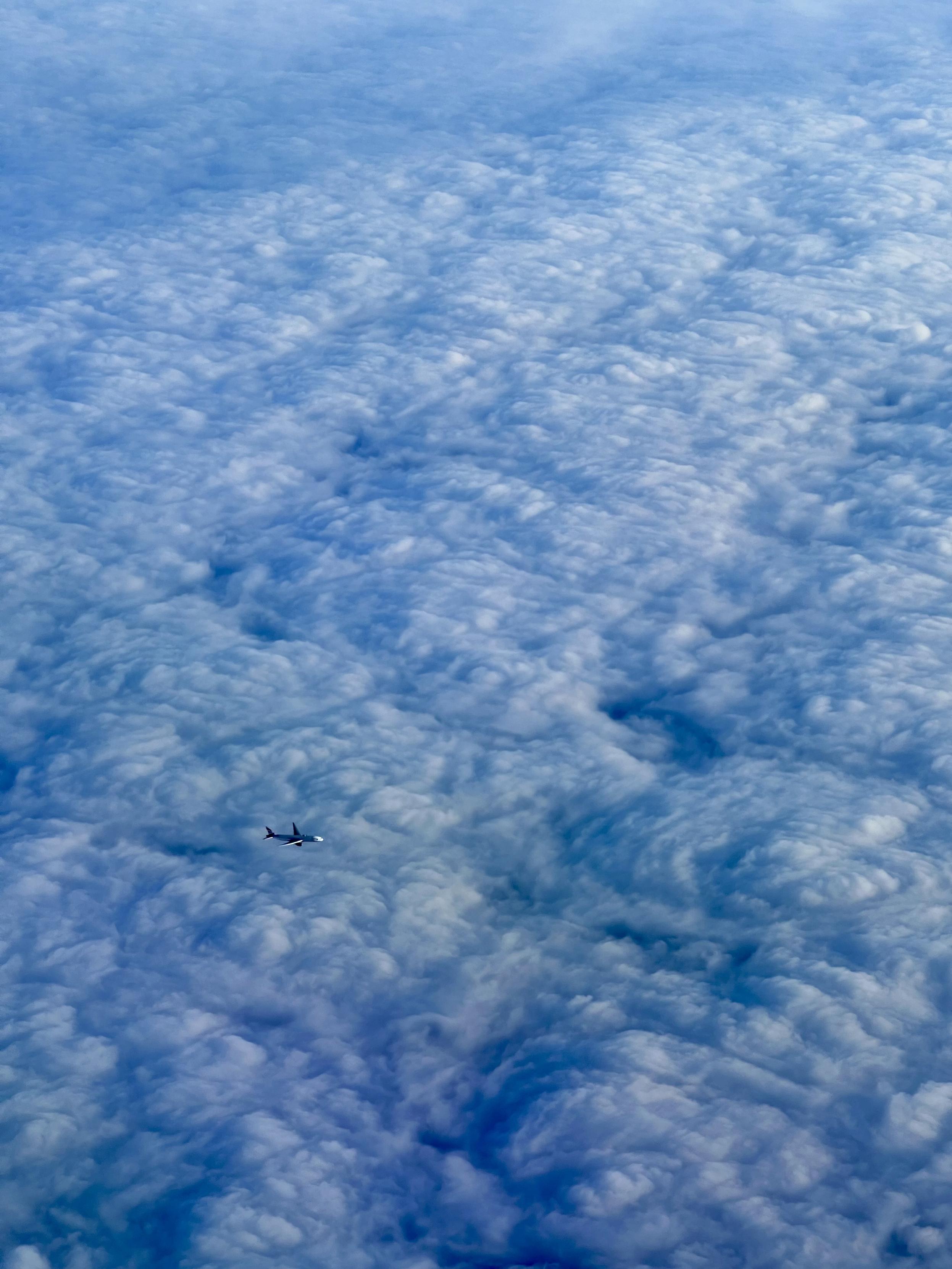 Fluffy clouds from above. In the bottom left hand corner is a passenger jet travelling from left to right.