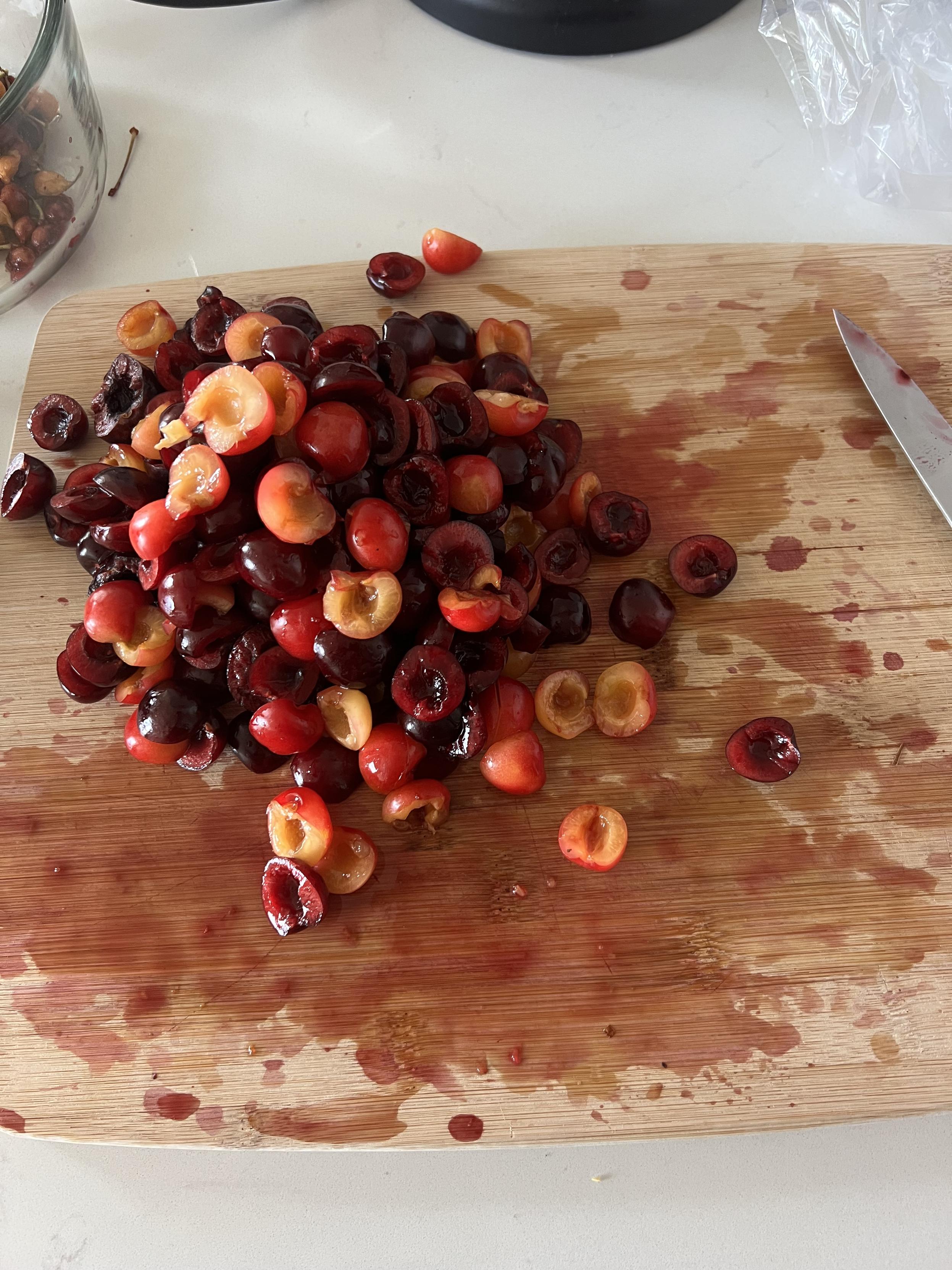 A pile of halted and pitter cherries sitting on a bamboo cutting board. The cherry juice has stained the board purple.
