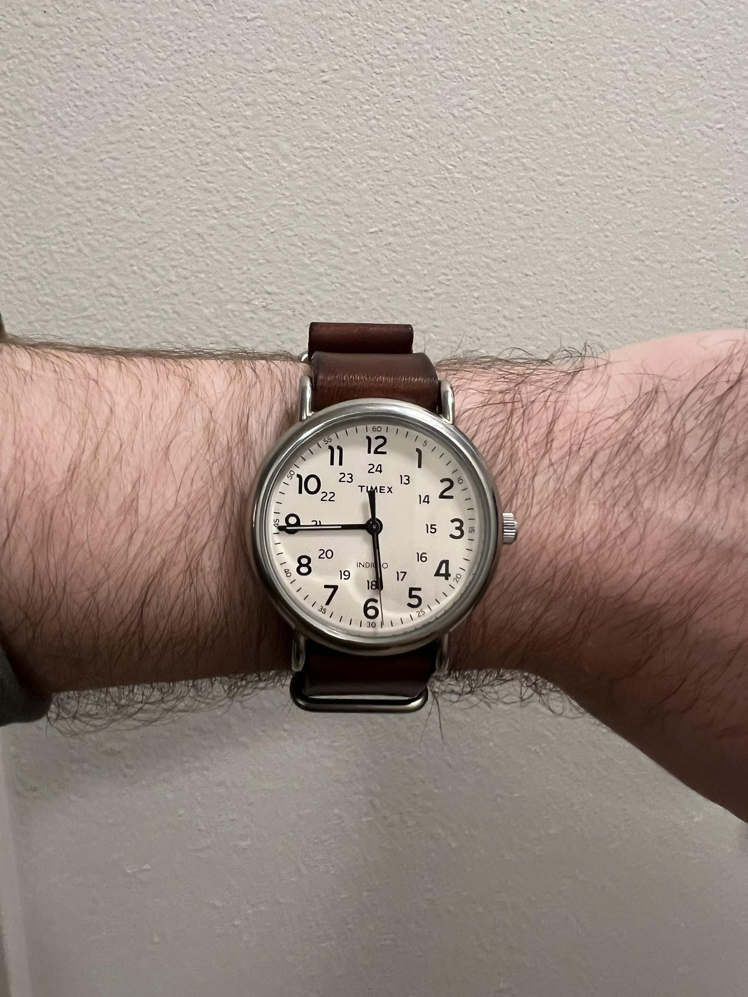 A cream faced Timex Weekender watch on my wrist. The strap is brown leather.The watch indicates 5:45.