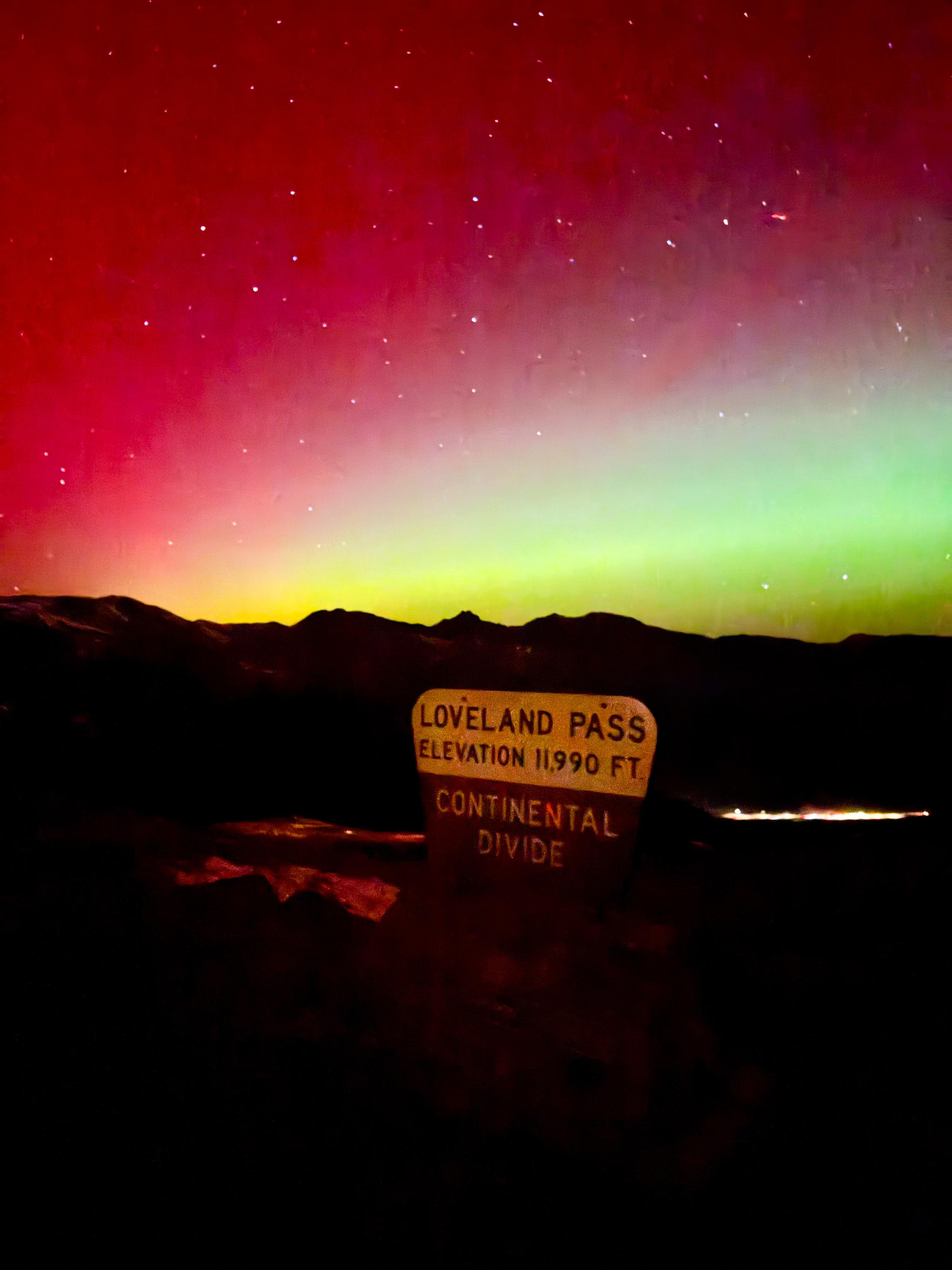 Aurora Borealis over a sign that says LOVELAND PASS, ELEVATION 11,990 FT, CONTINENTAL DIVIDE