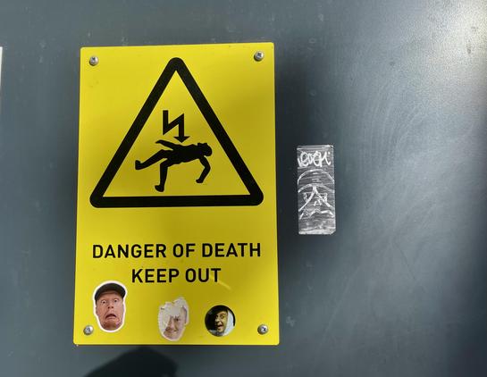 A danger of death sign but with stickers of people’s faces stuck on it. 