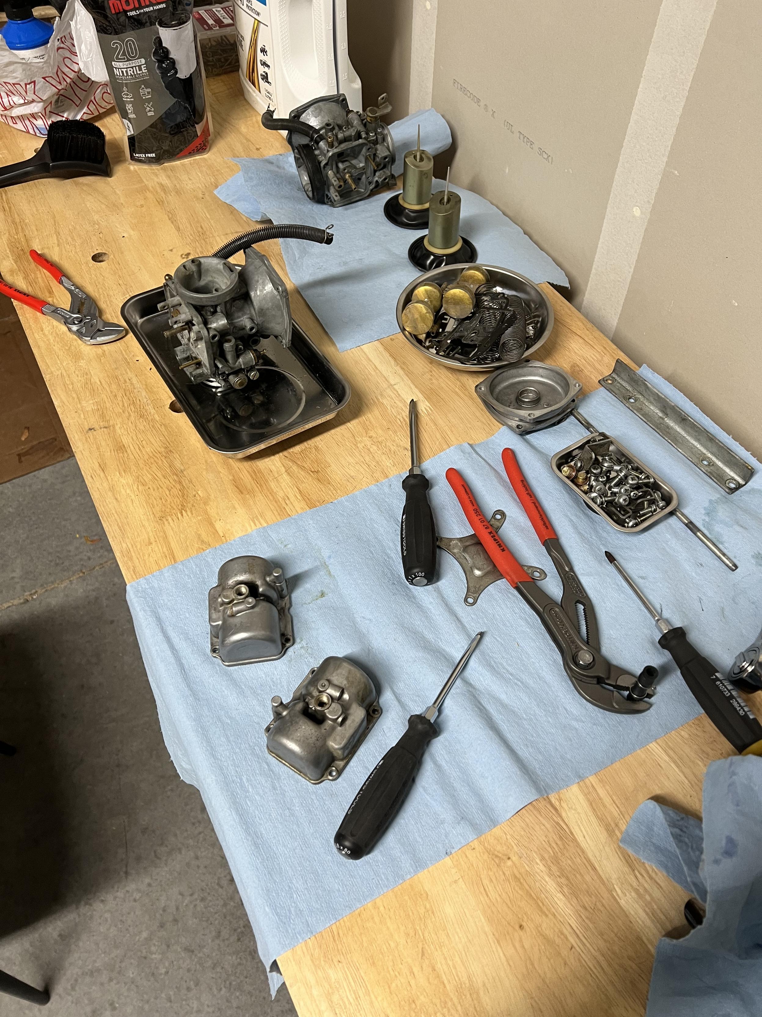 A work bench with various tools and carburettor components laying on blue paper towels.