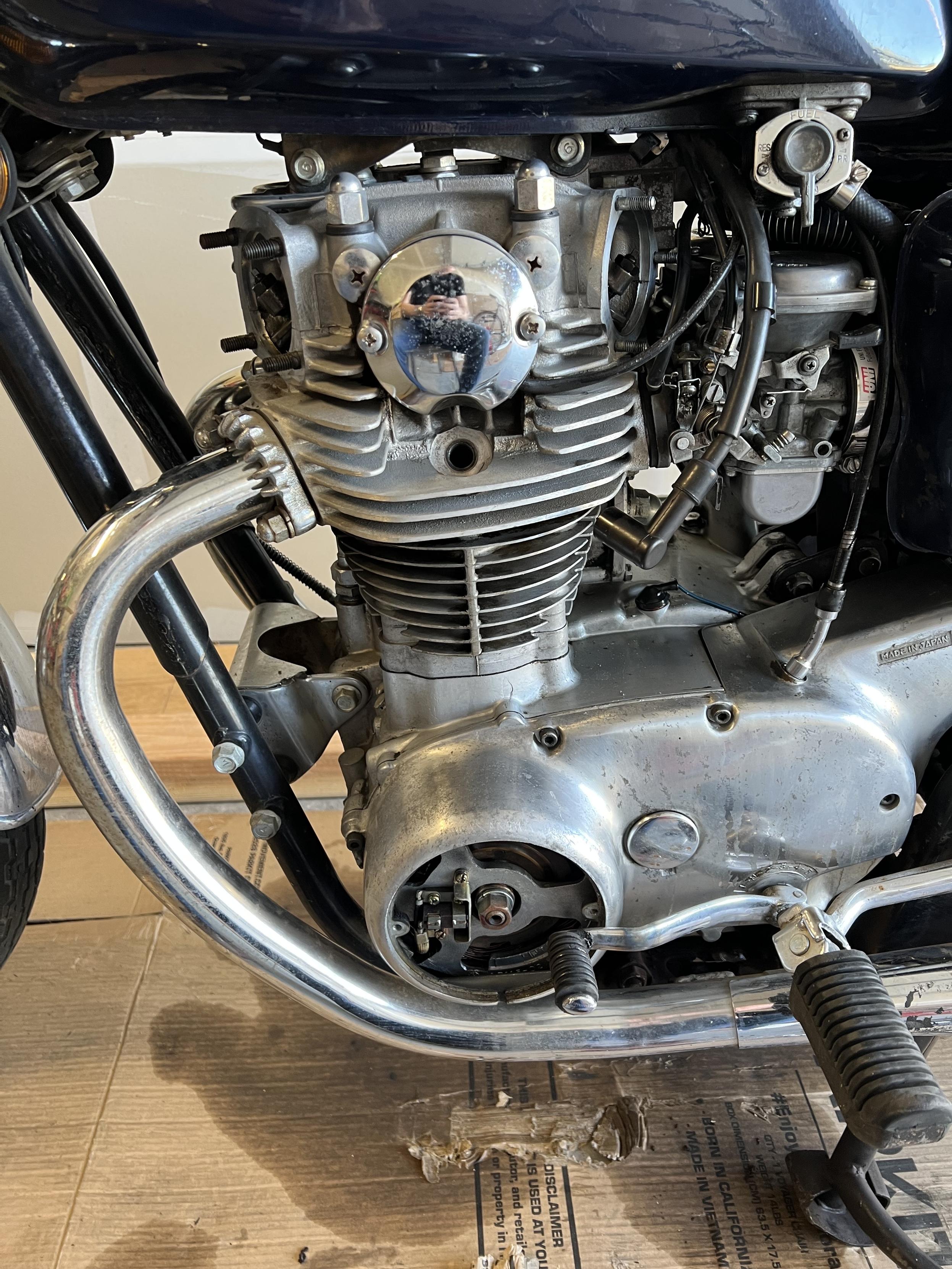 A close up shot of a motorcycle engine. The valve covers have been removed and long with the timing inspection cover.