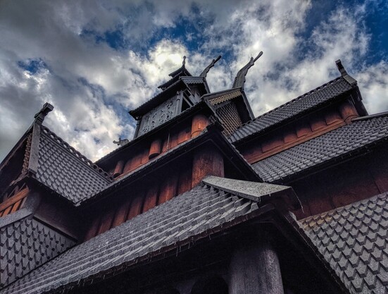 The intricate, multilayered roof of a dark wood stave church and the blue sky behind it