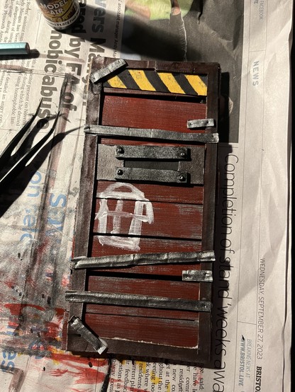 A 1:12 door reinforced with steel bars, painted in red. There's a reinforced window in middle and a pictogram of a house painted on it in white 