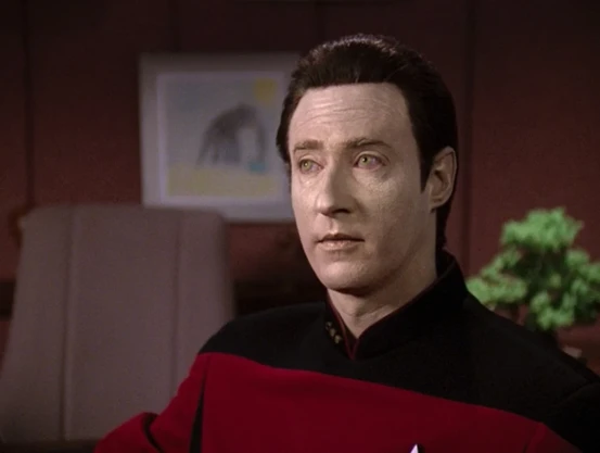 Data as portrayed by Brent Spiner. He is a male humanoid android with white/gold skin, yellow eyes, and dark brown hair.