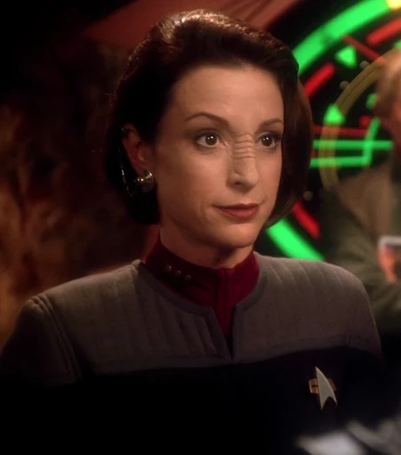 Kira Nerys as portrayed by Nana Visitor. She is a white Bajoran woman with ginger hair (here cut into a bob) and the standard Bajoran nose ridges and earring. She has a piercing gaze.