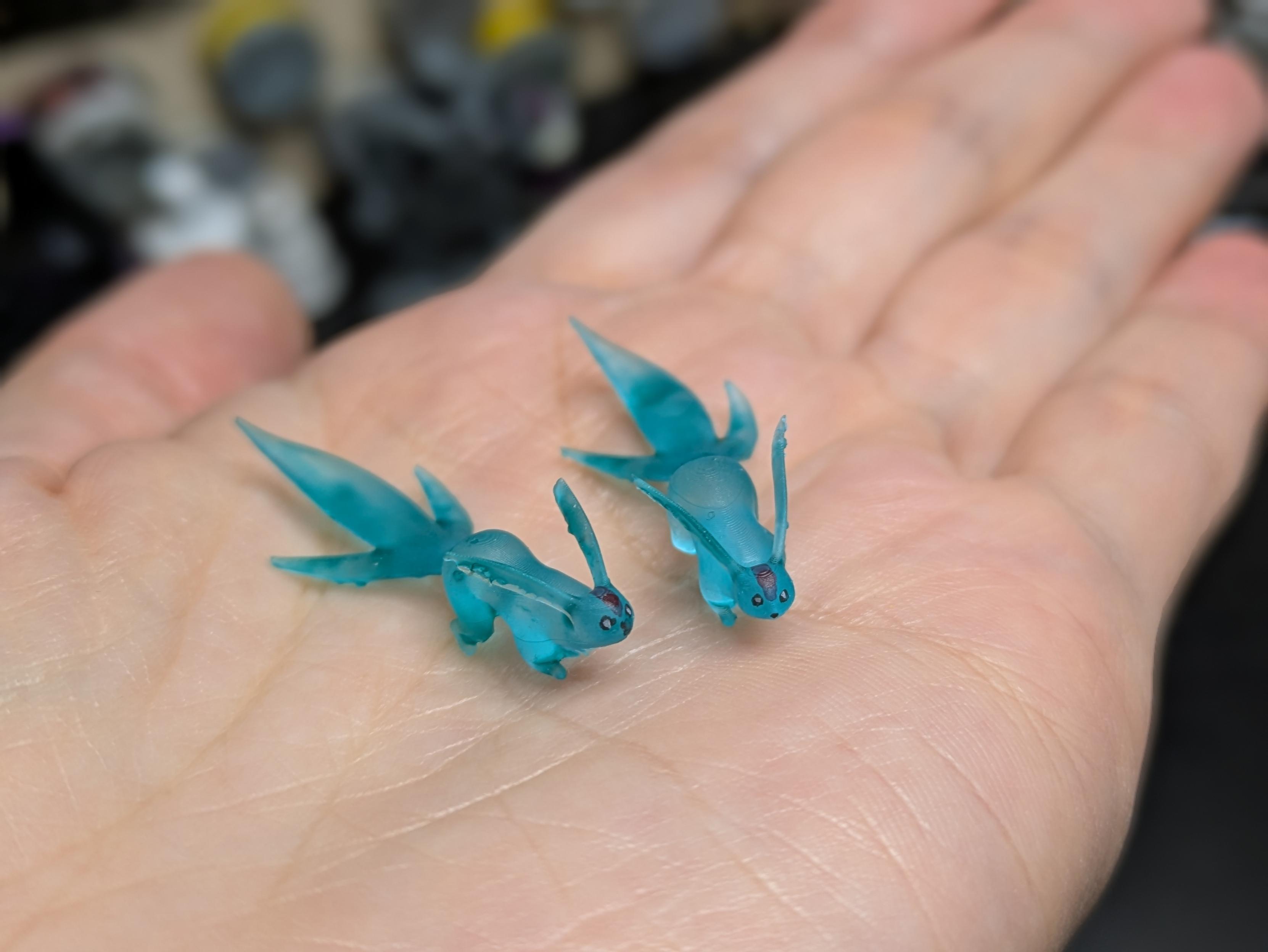 The same pair of figurines, shown perching on an open palm. They are 2cm long, tops.