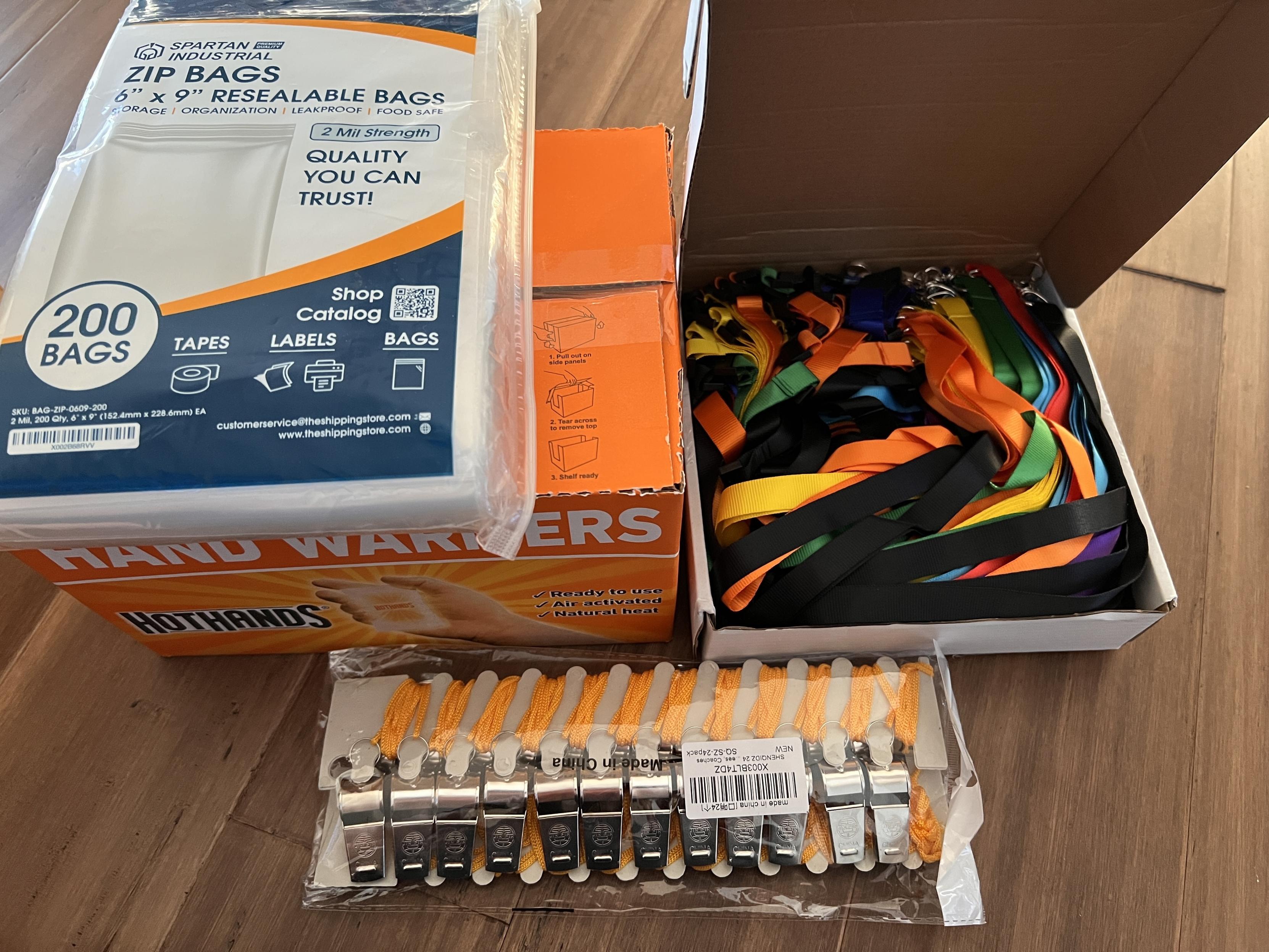 Photo showing boxes of plastic bags, handwarmers, multicolored lanyards, and a bag full of whistles.