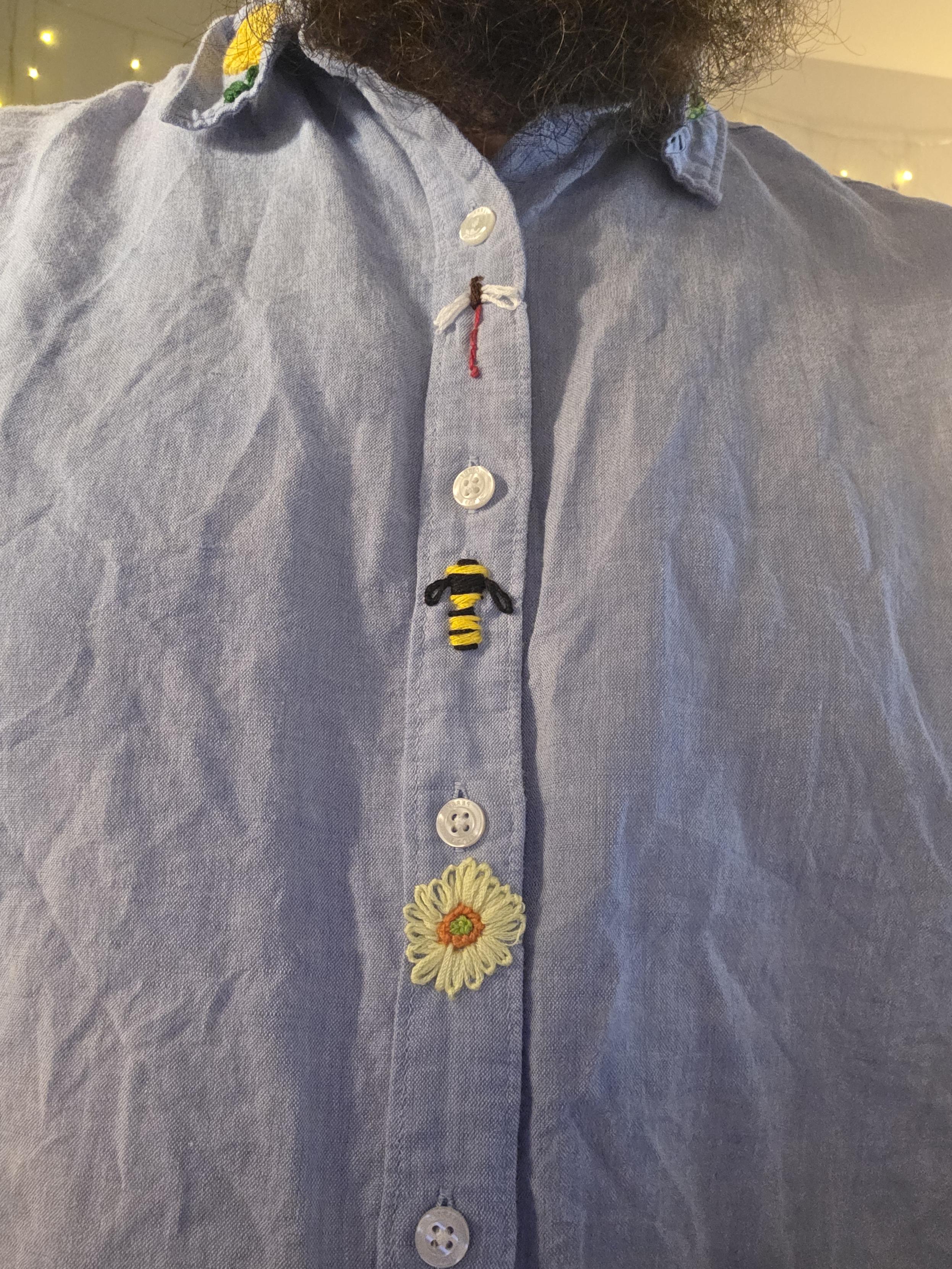 Embroidery of a Dragonfly, a bee, and a flower on a shirt worn by a man with a beard