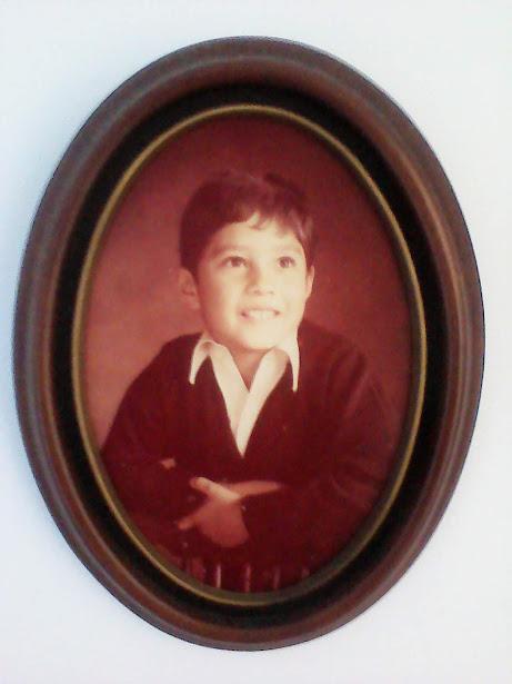 A very young Memento glamour pic, in an old timey wooden oval frame, smiling, unjaded, looking off into some bright future.