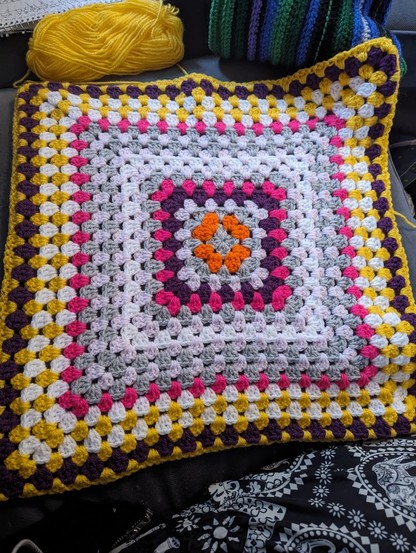 Crocheted blanket, variety of colours including grey, orange, white, pink, purple and yellow.