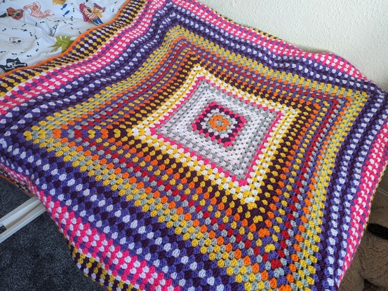 Very colourful crochet blanket. Featuring pink, purple, yellow orange, red and many more.