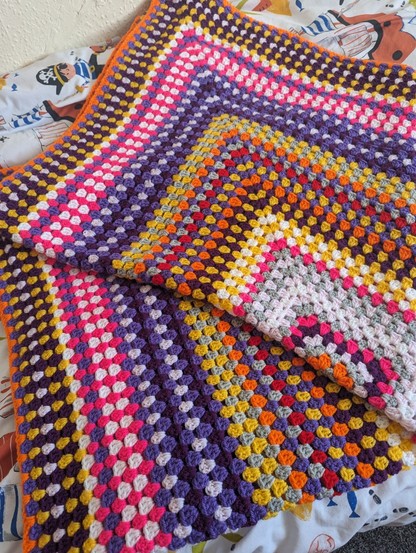 Close up of a very colourful crochet blanket. Featuring pink, purple, yellow orange, red and many more.