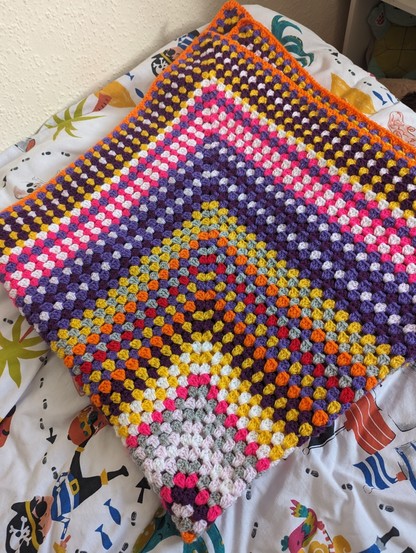 Very colourful crochet blanket. Featuring pink, purple, yellow orange, red and many more.