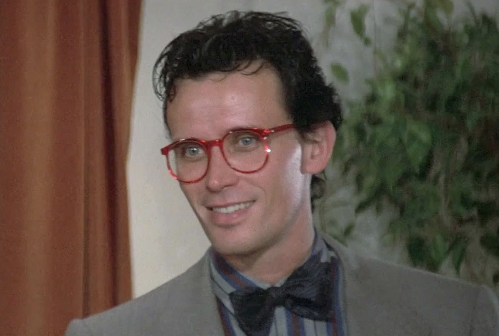 photo of dr peter weller as dr buckaroo banzai, wearing a suit, bow tie, and red transparent-plastic rimmed glasses