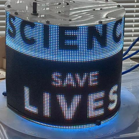 LED display wrapped around a top hat bearing a slogan about the value of science.