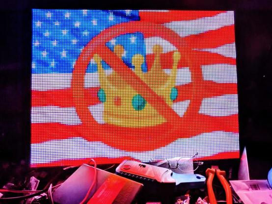 LED sign on a messy desk. Sign depicts a flag with some emoji in front of it.