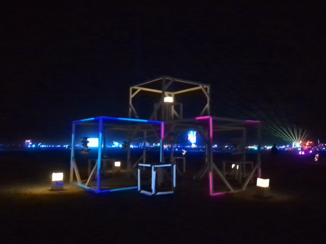 A set of open frame cubes. The outlines of three of the cubes have moving colors projected on them.