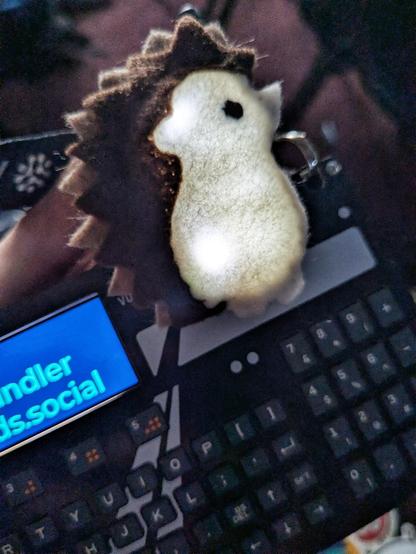 a glowing felt hedgehog on top of a Hackaday Supercon 2025 badge