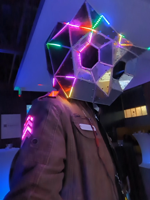 person wearing a reflective low poly owl mask, with LEDs along the edges moving in a pattern following the shapes.