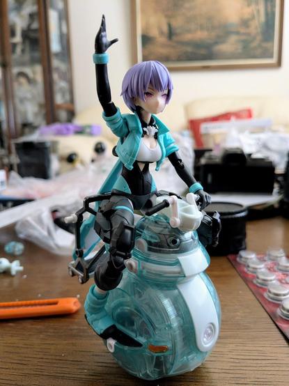 A purple haired anime-styled girl in a light teal & black outfit is riding atop a similarly colored robot scooter.