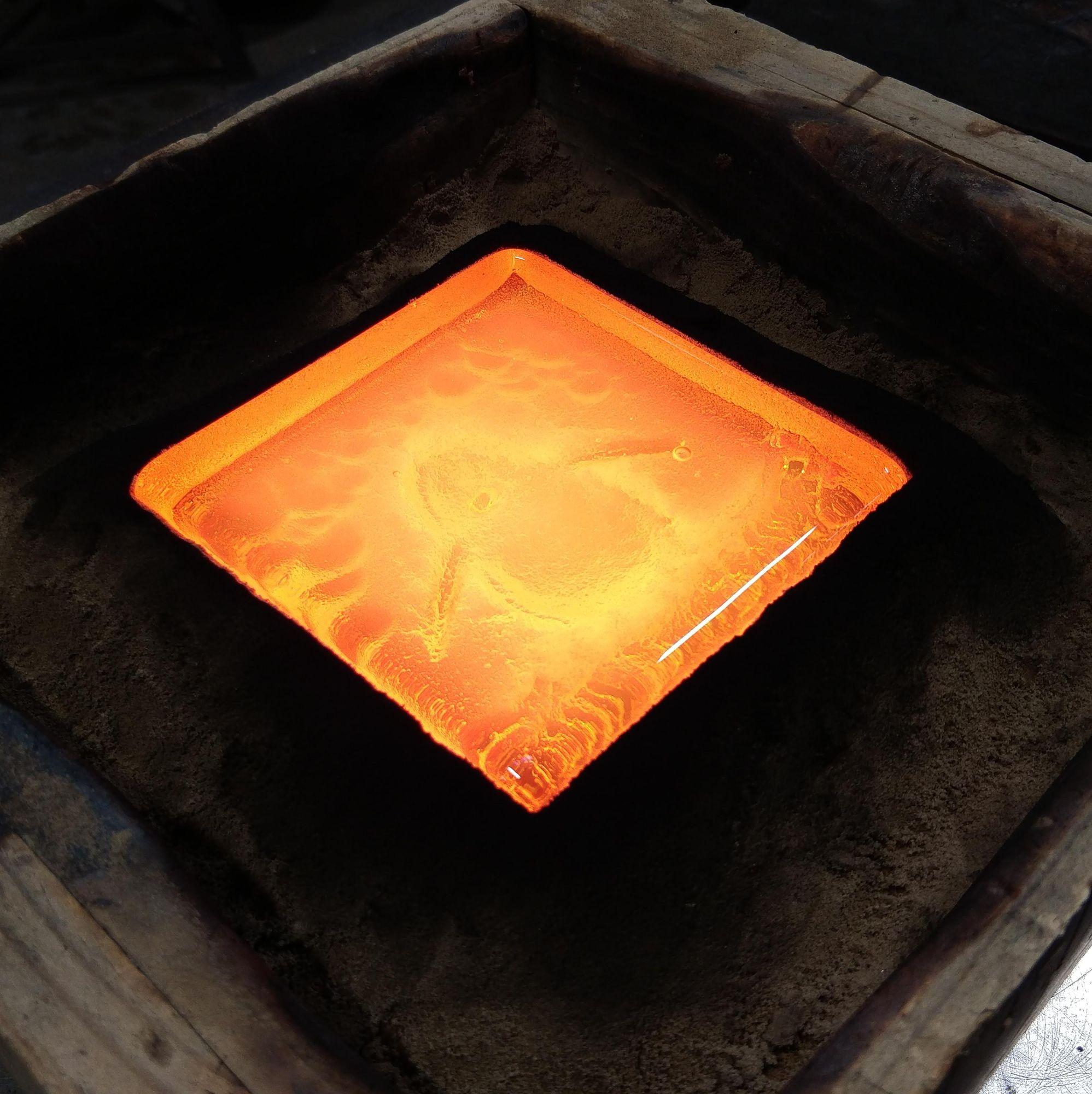 molten glass glowing orange in a square sand mold